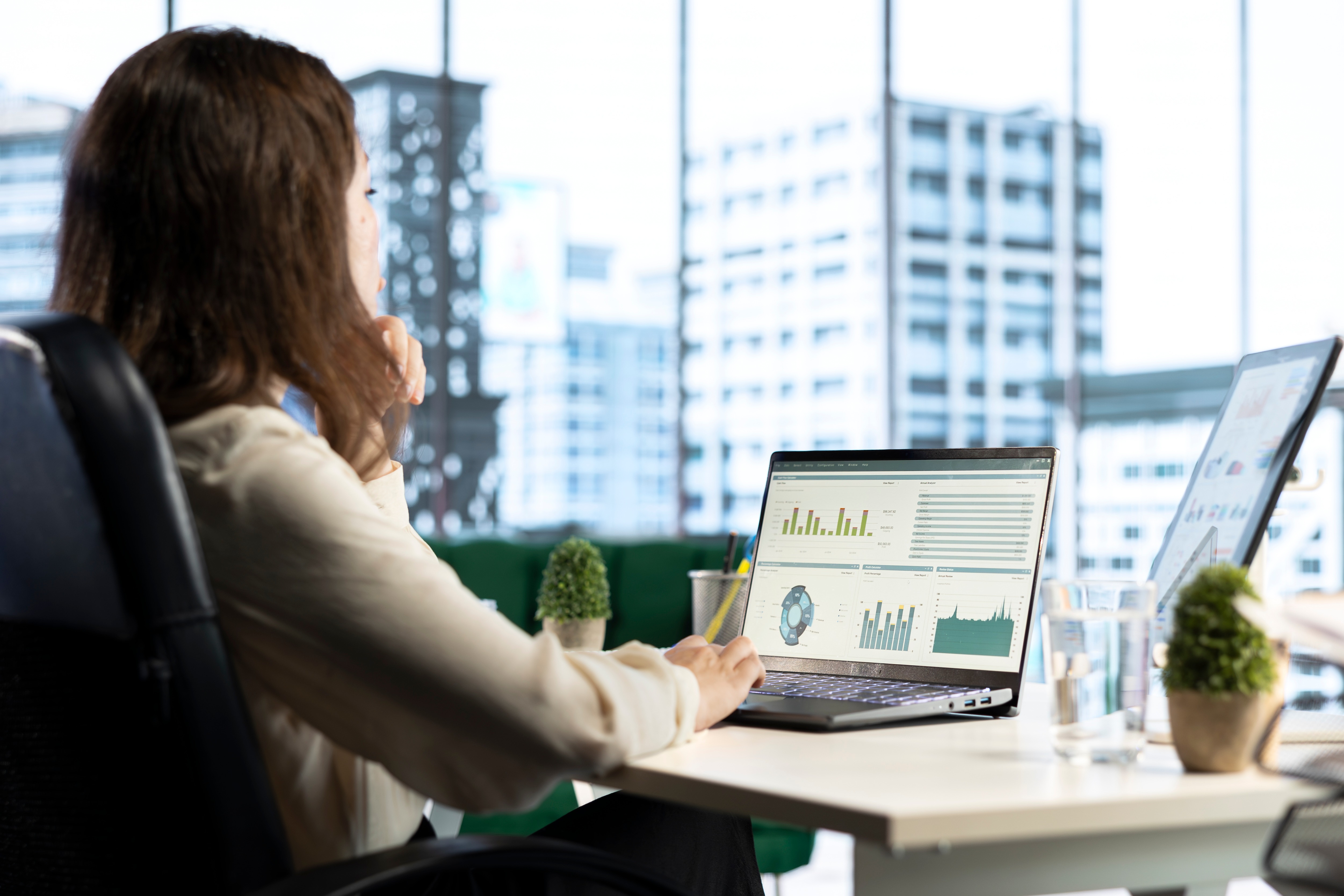 Professional woman analyzing business data and charts on laptop in modern office