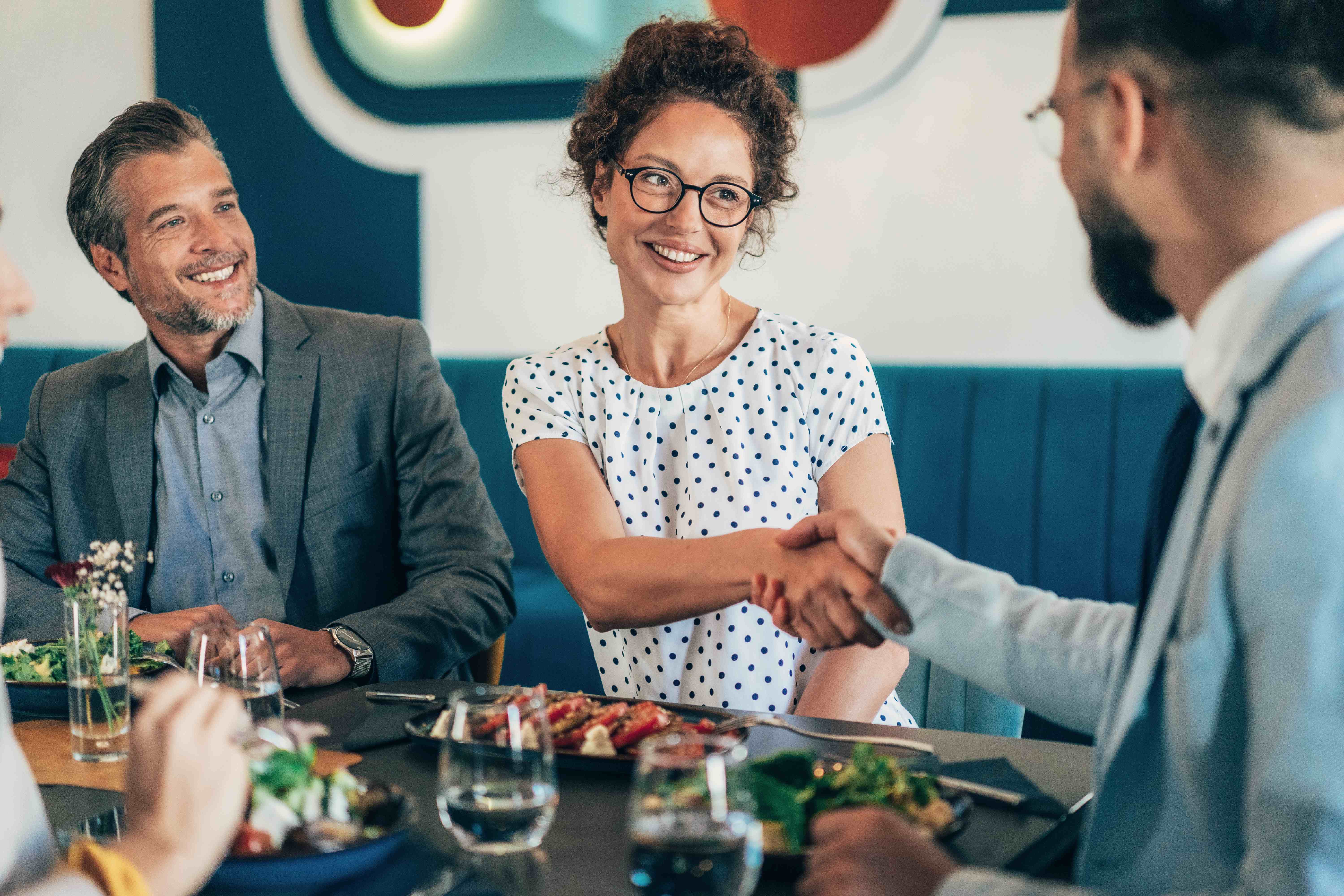 Business professionals shaking hands during acquisition meeting at restaurant lunch