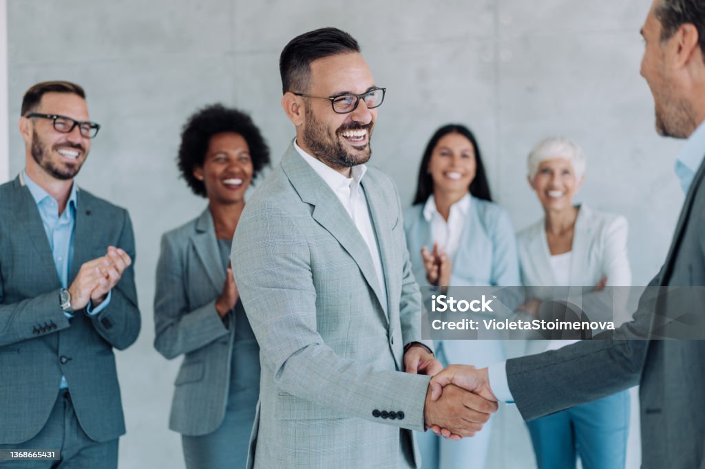 Diverse business team celebrating successful acquisition with handshake and smiling professionals